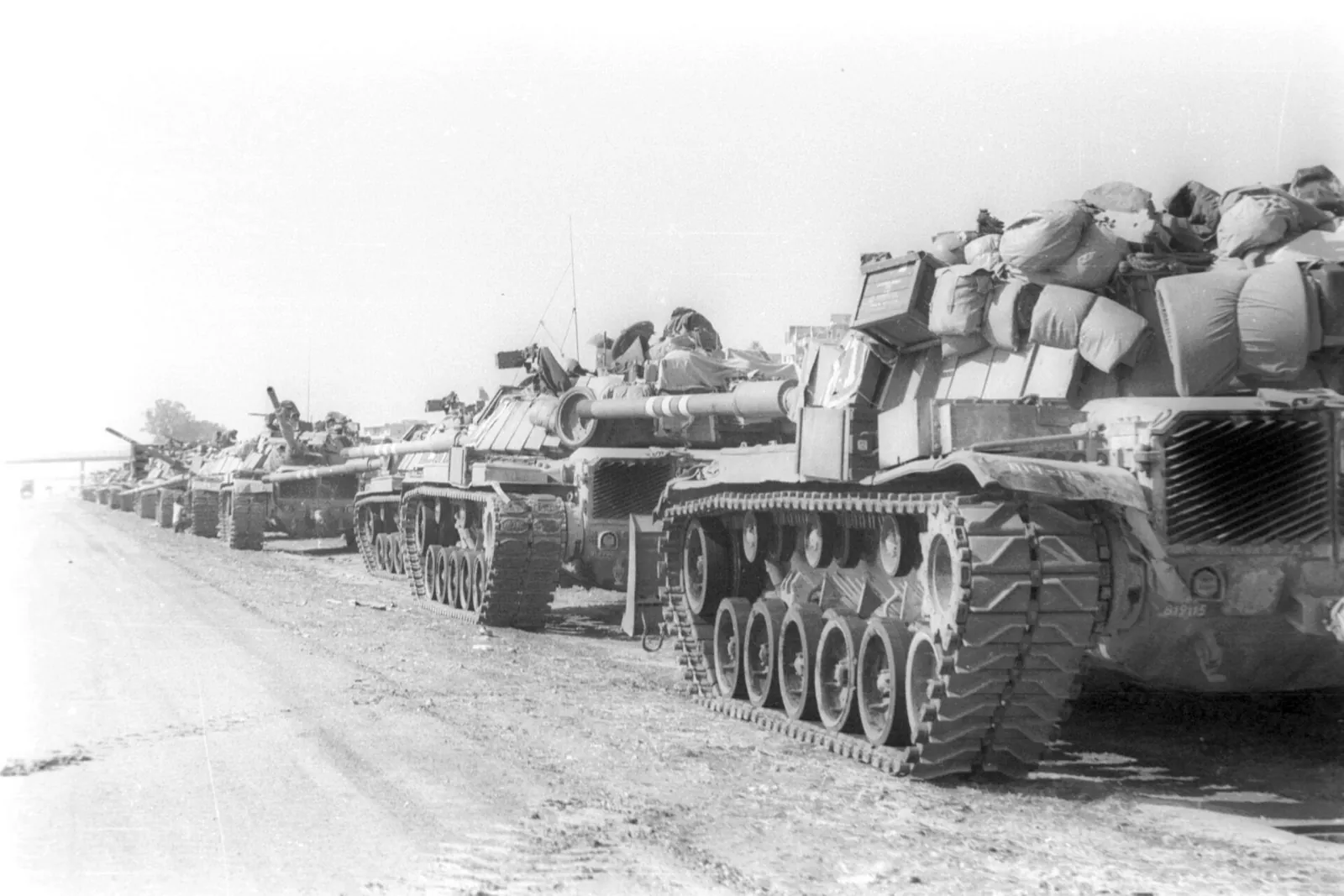 A column of Israeli tanks loaded with gear parked along a dusty road