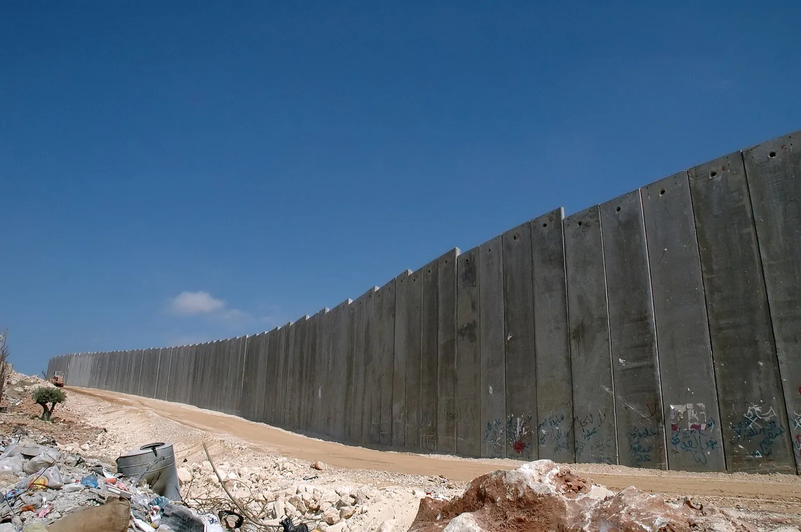 A tall concrete wall of the separation barrier curving across rocky ground